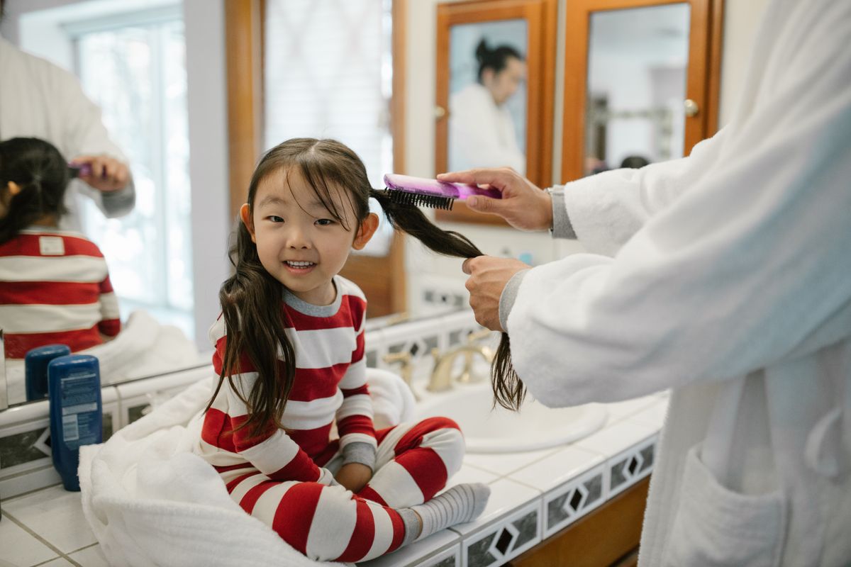 A father combing his daughter's hair during their morning routine