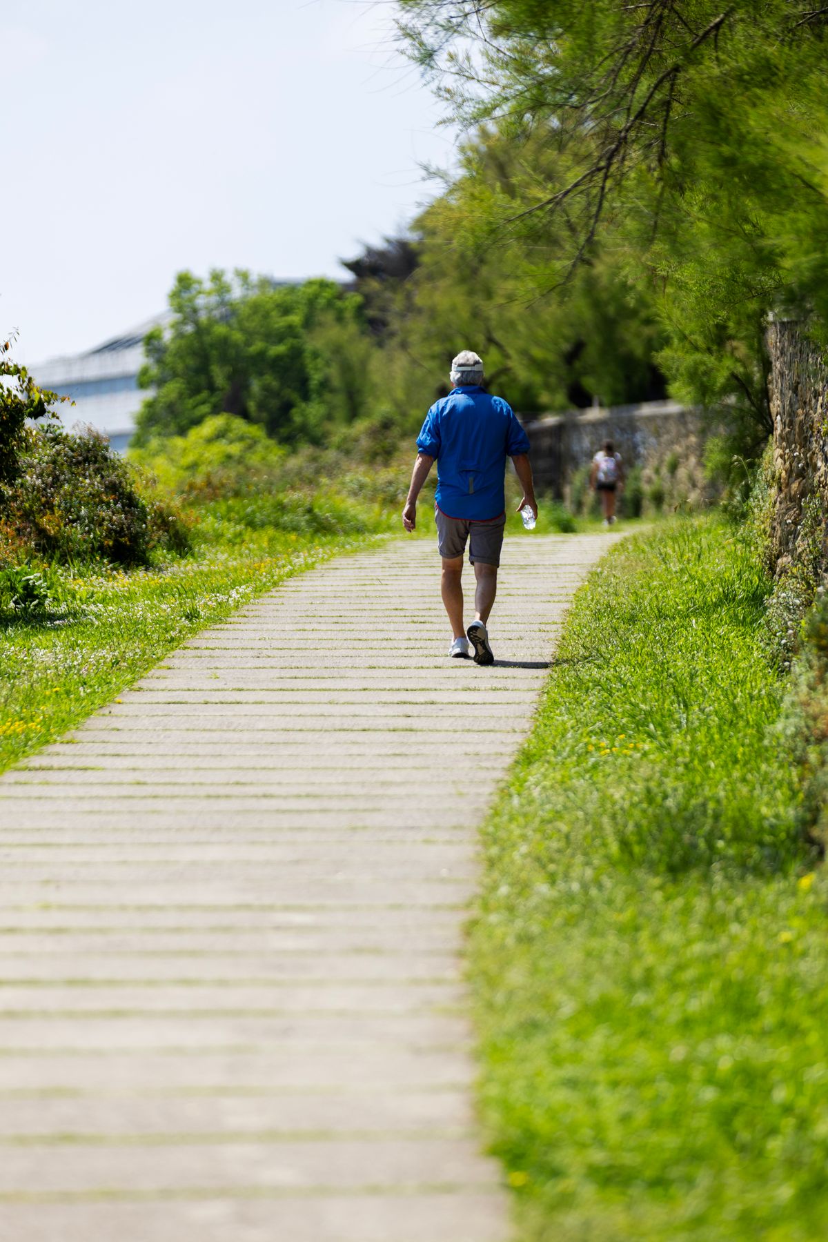 A man walking along a sunlit green pathway